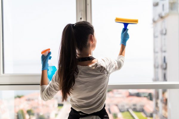 people, housework and housekeeping concept. Happy woman in gloves cleaning window with rag and cleanser spray at home people, housework and housekeeping concept - happy woman in gloves cleaning window with rag and cleanser spray at home